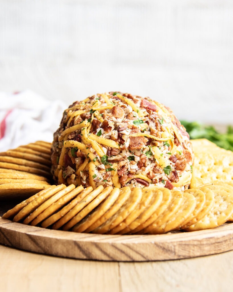 A plate of crackers surrounding a bacon ranch cheeseball.