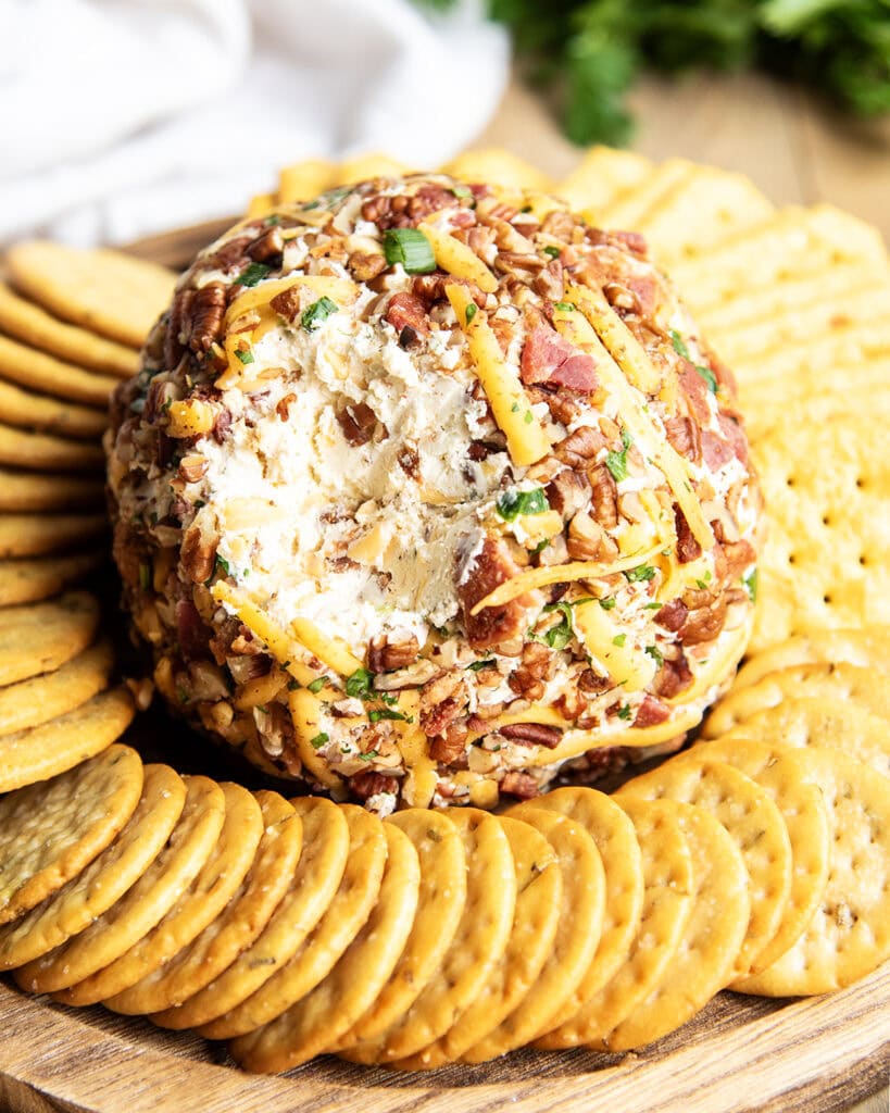 A bacon and cheddar cheese covered cheese ball with some of the outside taken out to show the center.