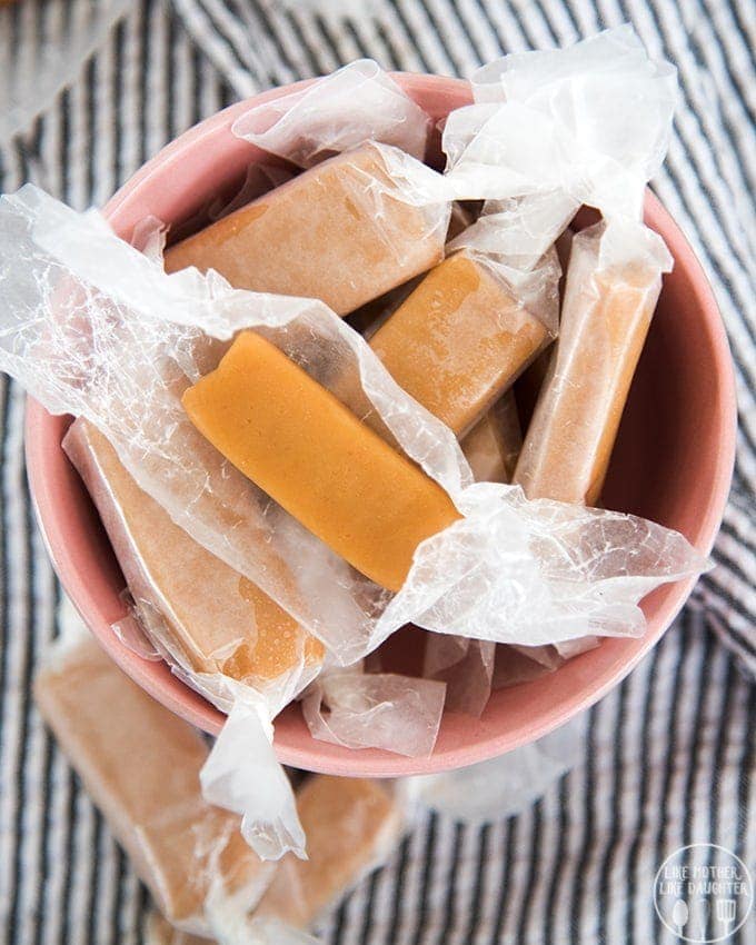 A bowl of homemade microwave caramels wrapped in waxed paper. 