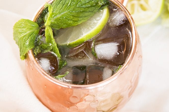 A copper mug full of ice, a lime slice, and fresh mint leaves.