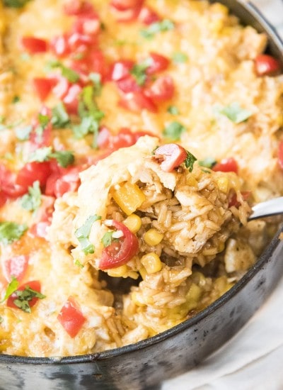 A close up of a scoopful of enchilada rice casserole being lifted out of a skillet.