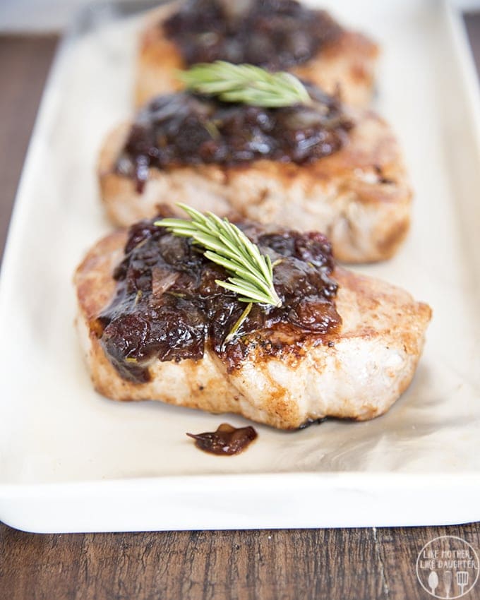 A plate of pork chop pieces with a cranberry glaze, and a sprig of fresh rosemary on each.