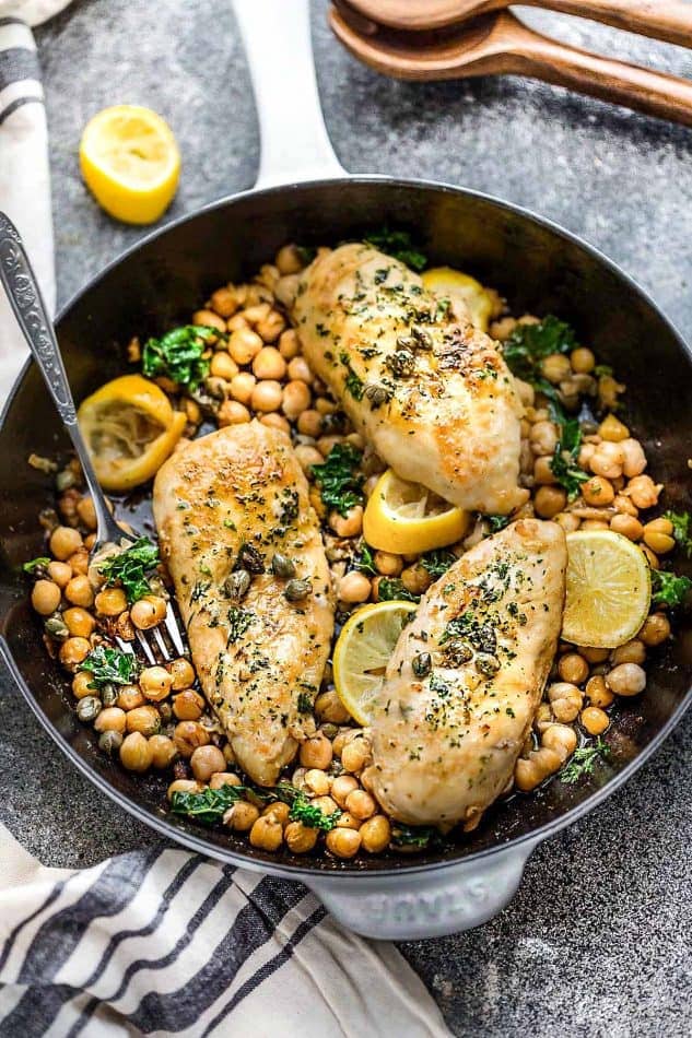 A skillet full of three chicken piccata breast with chick peas and lemon slices.