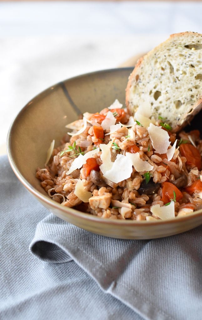 A bowl of farro and chicken topped with tomatoes and parmesan cheese. 