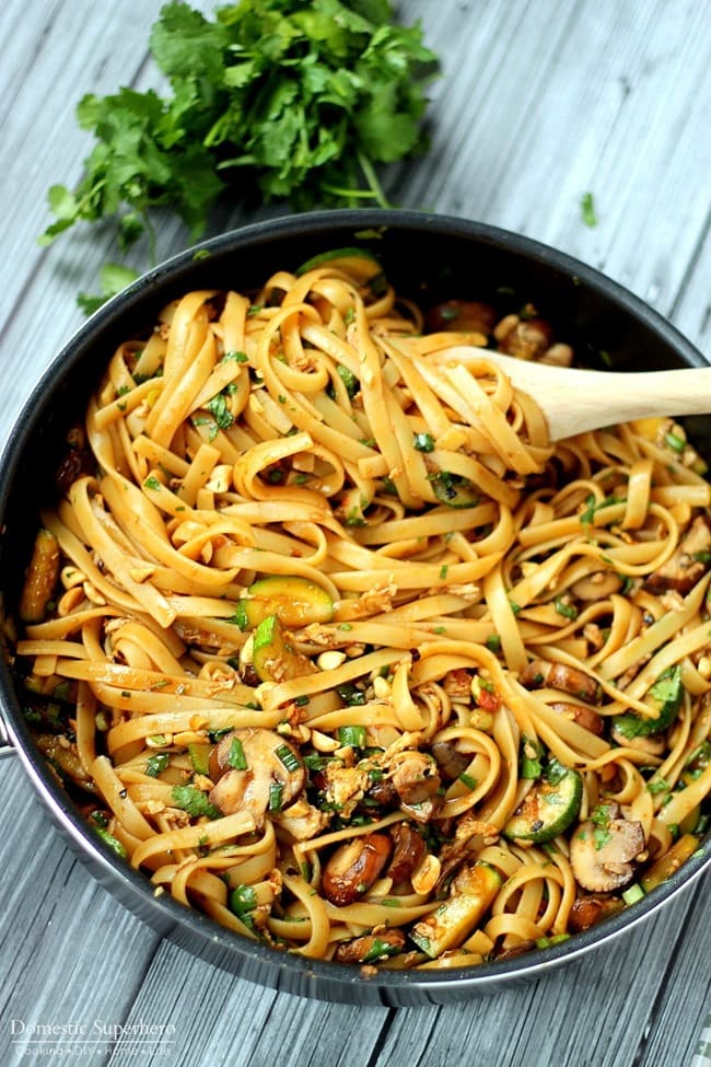 A skillet full of spicy thai noodles with mushrooms and cilantro.