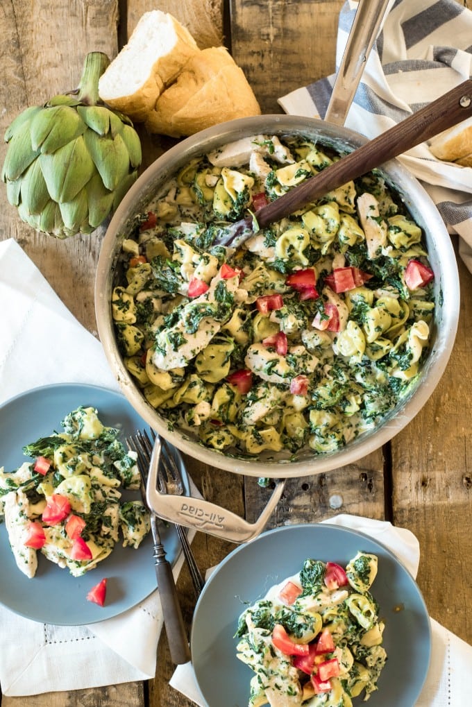 A large bowl of spinach and artichoke dip tortellini pasta with bell peppers. 