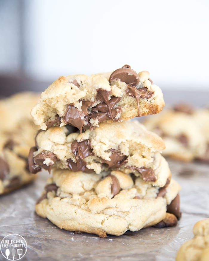 A stack of large chocolate chip cookies, the top cookie is broken in half showing the melted chocolate chips.