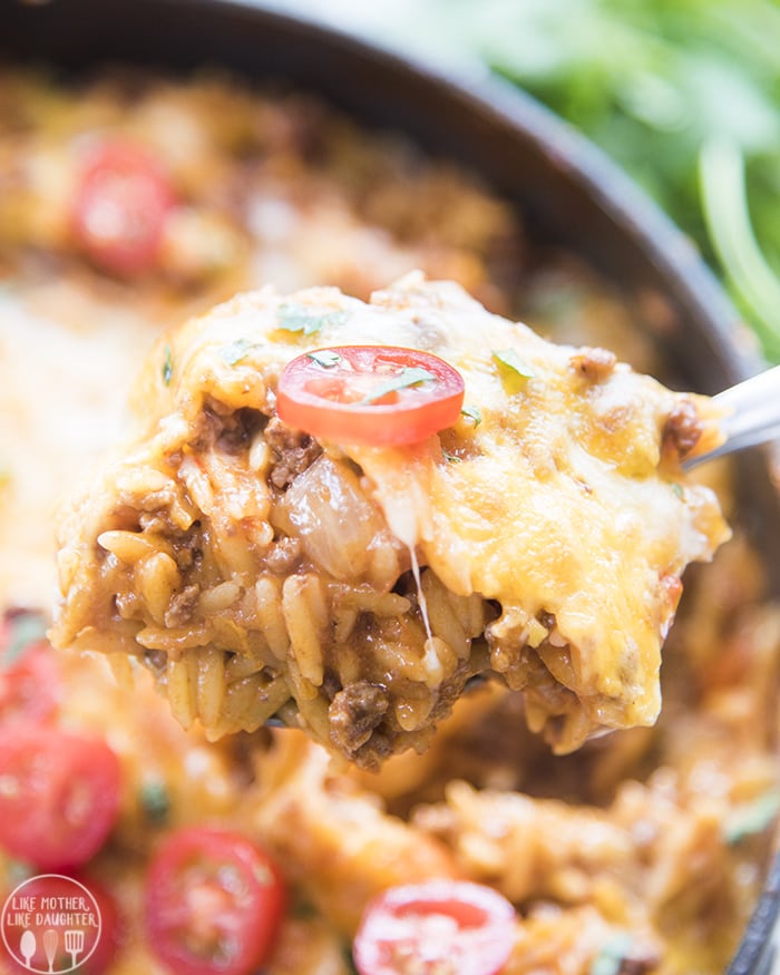A spoonful of one pot taco pasta topped with cheese and a slice of a cherry tomato.
