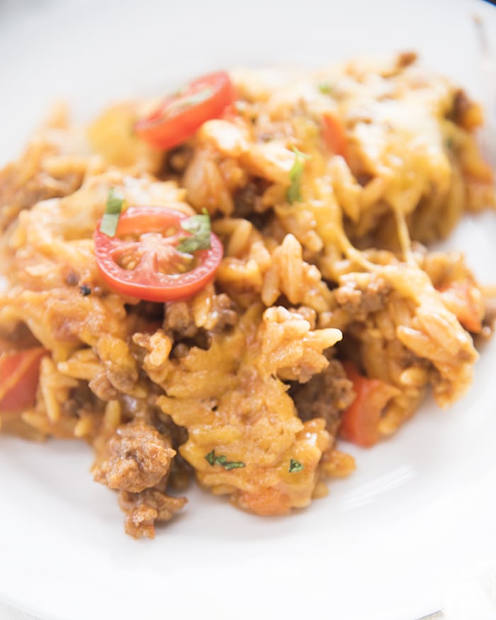 A serving of cheesy orzo pasta topped with diced tomatoes and cilantro.