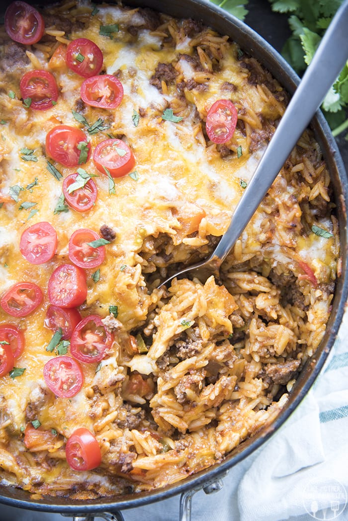 A pan of one pot taco pasta topped with cheese and halved tomatoes.