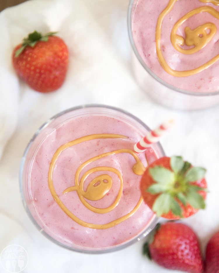 An overhead photo of two glasses of strawberry and peanut butter smoothie with peanut butter swirled on top.