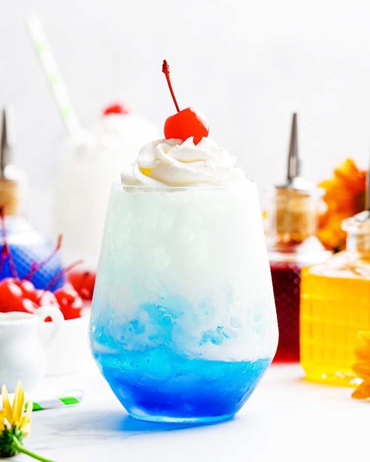 A blue colored Italian cream soda topped with whipped cream and a maraschino cherry.