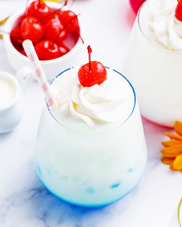 A blue colored Italian cream soda topped with whipped cream and a maraschino cherry.