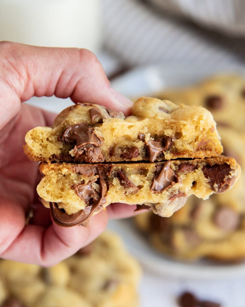 A hand holding two halves of a chocolate chip cookie with melted chocolate chips in the middle. 