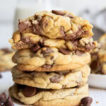 A stack of thick levain style chocolate chip cookies, with one broken in half showing the gooey center on top.