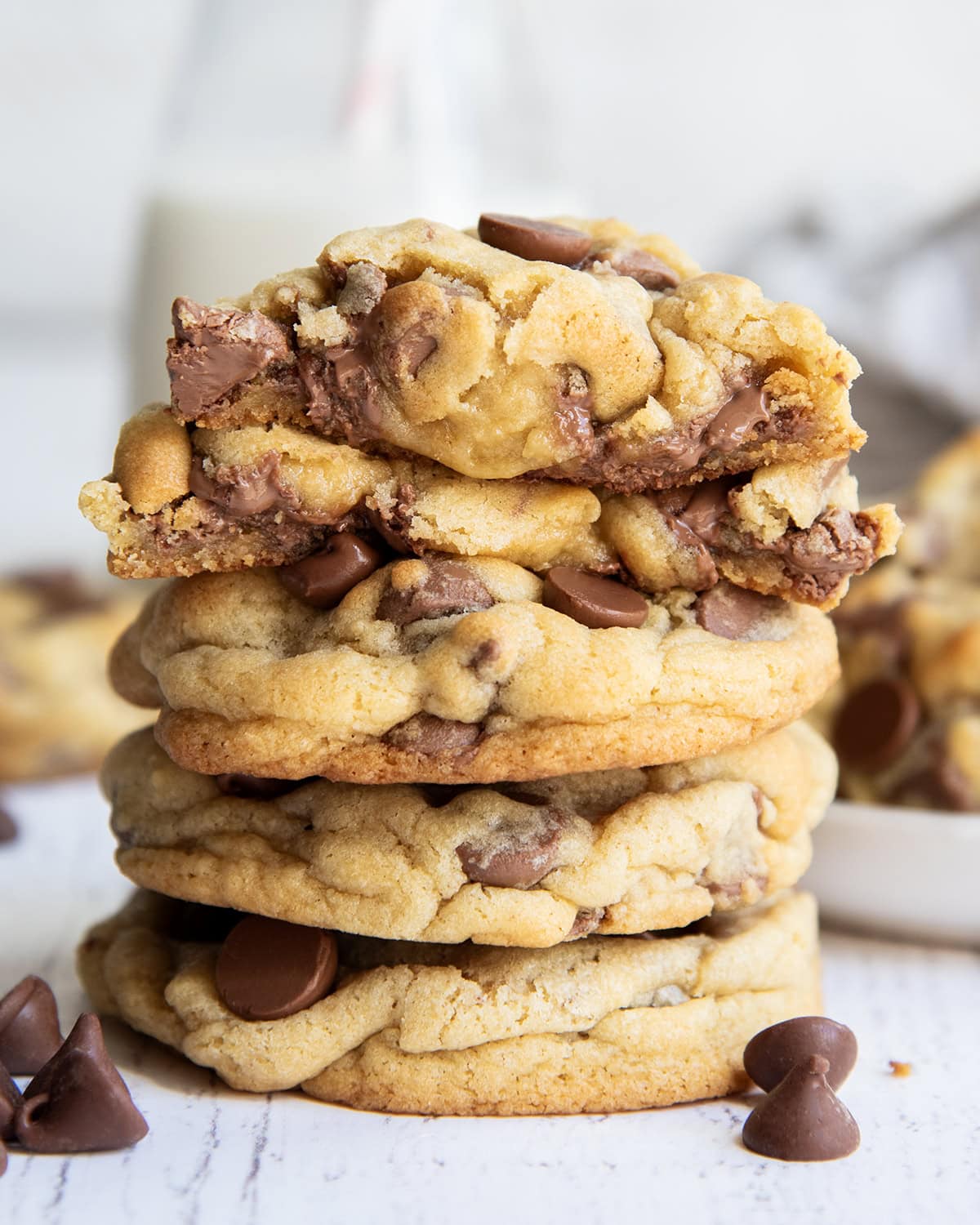 A stack of thick levain style chocolate chip cookies, with one broken in half showing the gooey center on top.