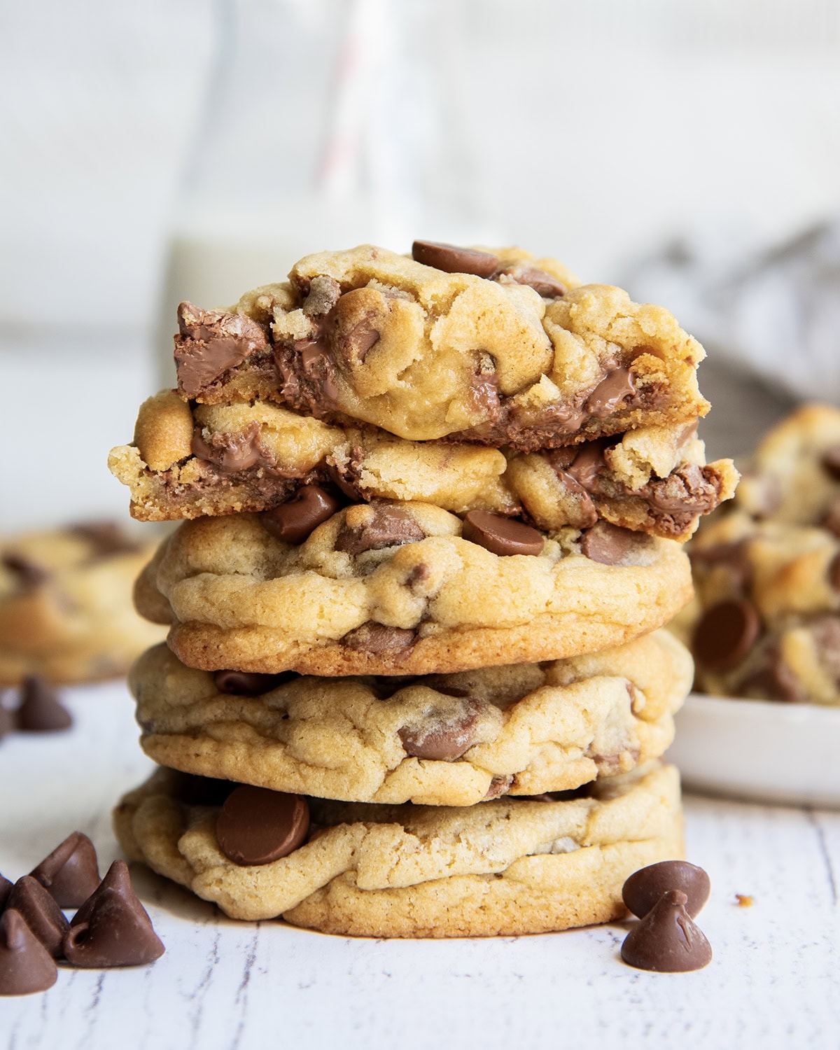 A stack of thick levain style chocolate chip cookies, with one broken in half showing the gooey center on top.