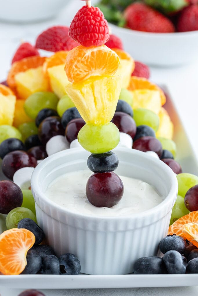 A rainbow fruit skewer dipping into a bowl of fruit dip.