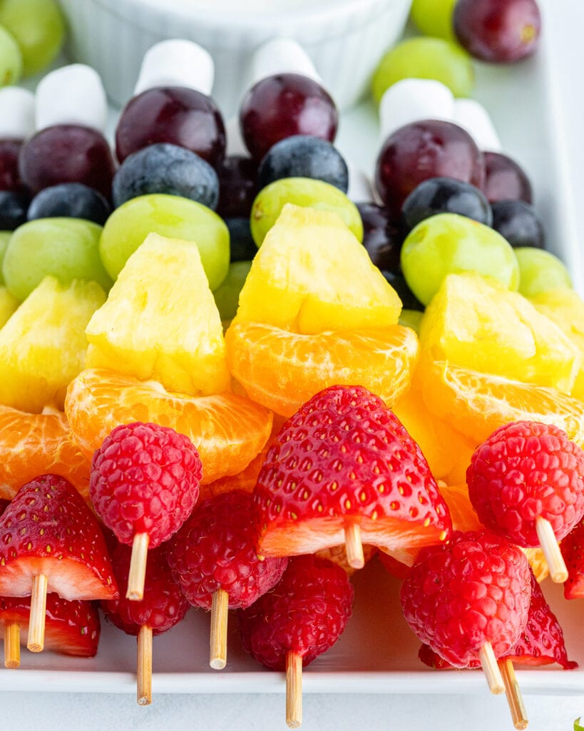 A pile of rainbow fruit kabobs on a tray.