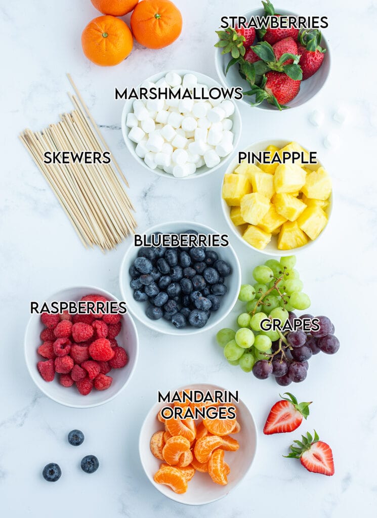 An overhead photo of bowls of fruit, and wooden skewers to make fruit kabobs.