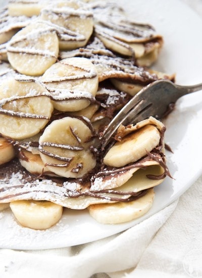 Stacks of crepes topped with banana slices and drizzled with chocolate.
