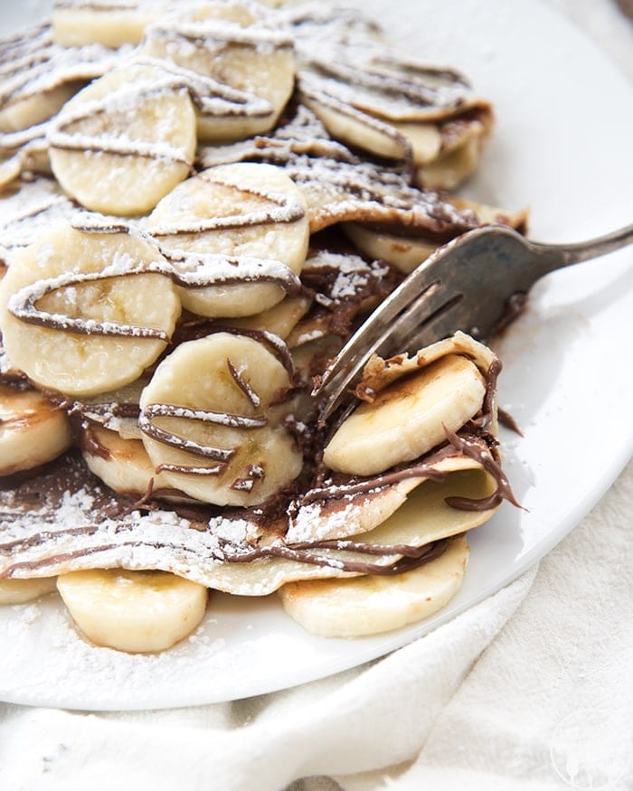 Stacks of crepes topped with banana slices and drizzled with chocolate.