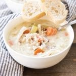 A bowl of creamy chicken and rice soup with two pieces of bread on it.