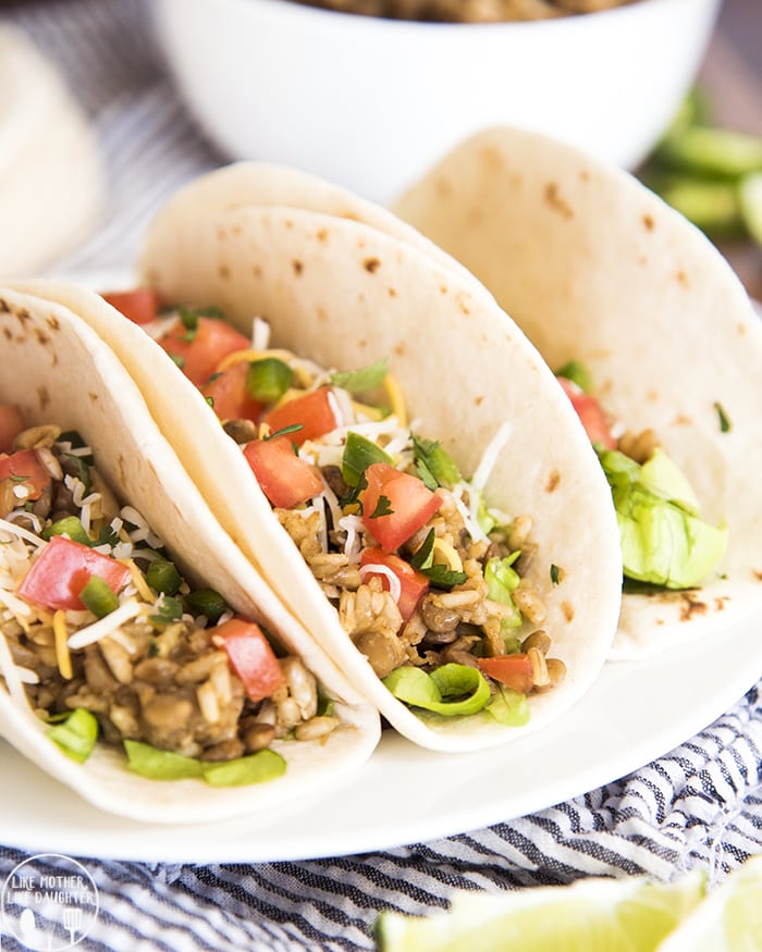 Three lentil tacos topped with lettuce and tomatoes on a plate. 