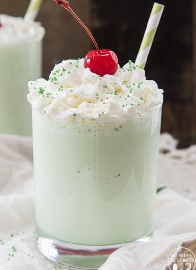 A green shamrock shake in a glass topped with whipped cream and a cherry.
