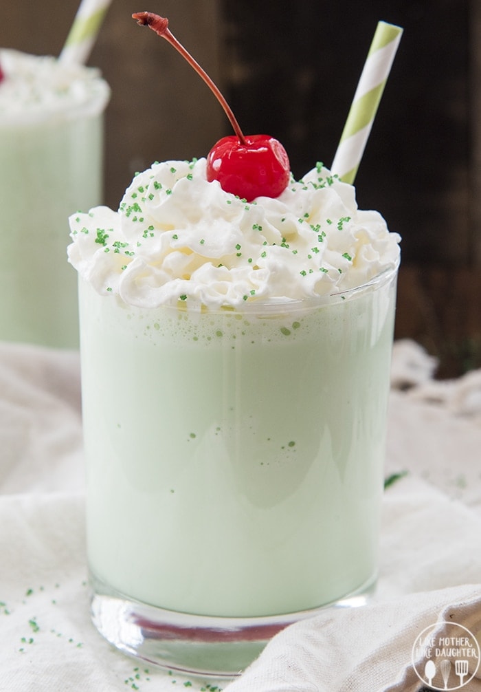 A green shamrock shake in a glass topped with whipped cream and a cherry.