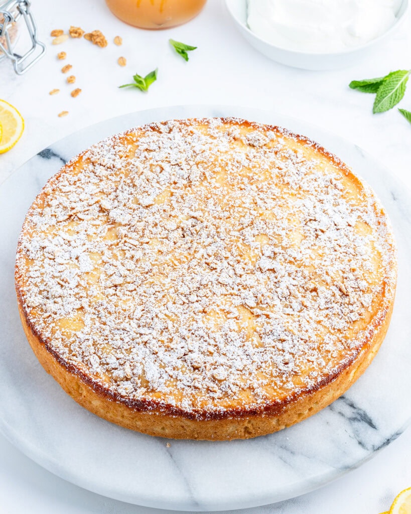 A marble plate topped with a round ricotta cake, topped with powdered sugar.