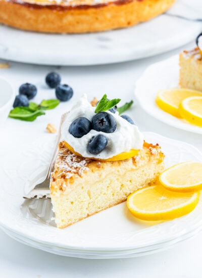 A piece of lemon ricotta cake topped with a dollop of whipped cream, three blueberries, and mint leaves.