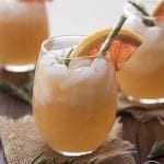 A glass of a grapefruit mocktail topped with rosemary and a grapefruit wedge.