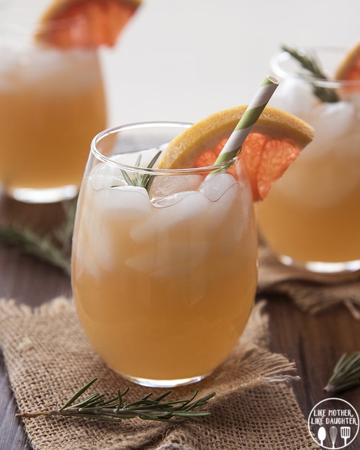 A glass of a grapefruit mocktail topped with rosemary and a grapefruit wedge.