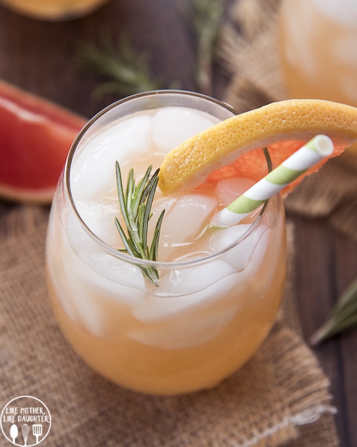 A glass of a sparkling grapefruit drink topped with fresh rosemary.