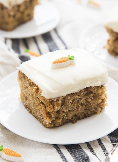 A square piece of carrot cake with cream cheese frosting on a plate.
