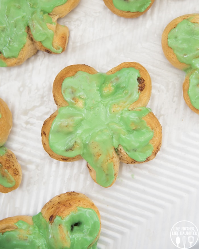 A cinnamon roll shaped like a four leaf clover with green frosting on top.