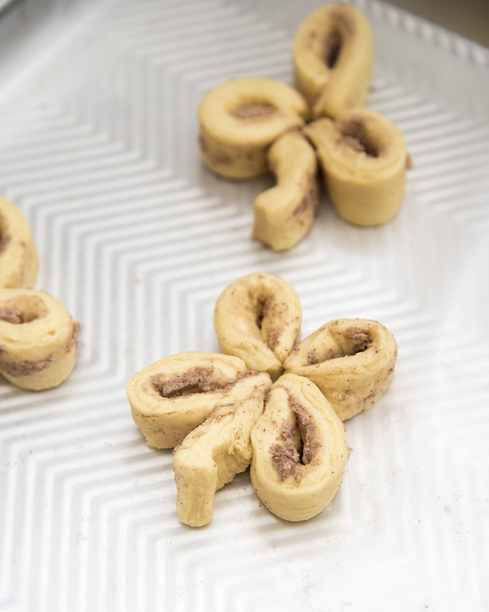Unbaked cinnamon rolls shaped like clovers on a baking pan.