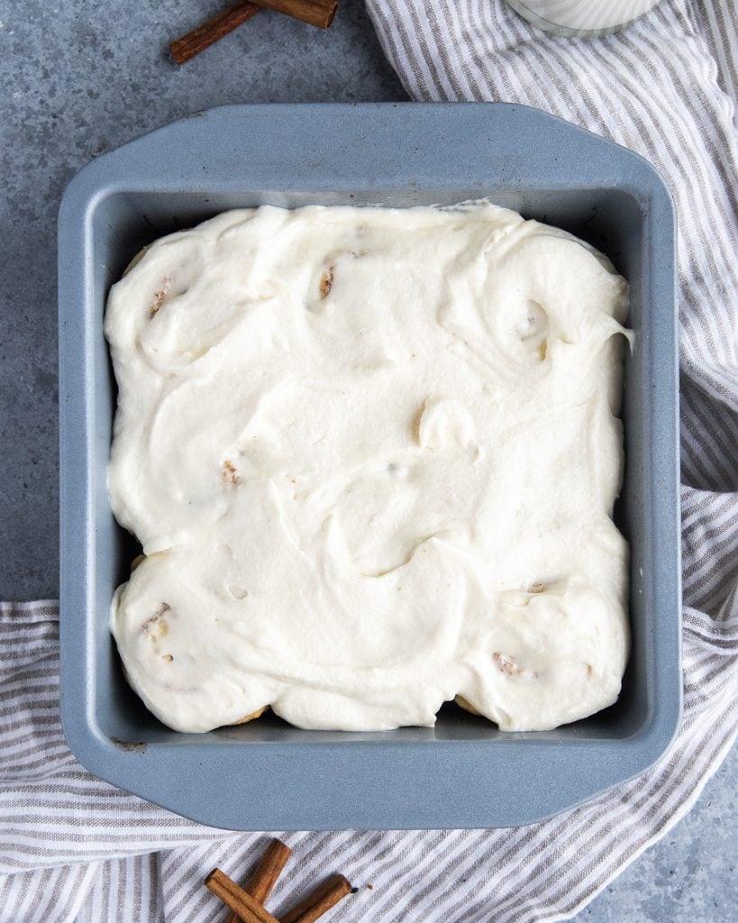 Cinnamon rolls in a pan topped with a thick layer of cream cheese frosting.