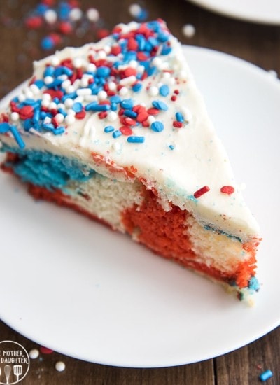 A slice of red white and blue swirled cake topped with white frosting and sprinkles.