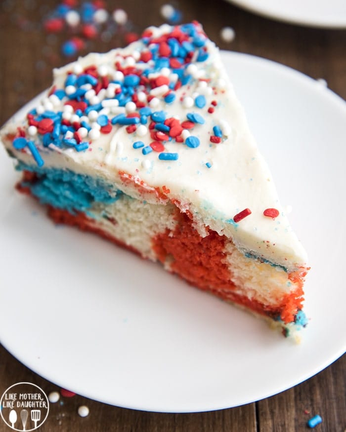A slice of red white and blue swirled cake topped with white frosting and sprinkles.