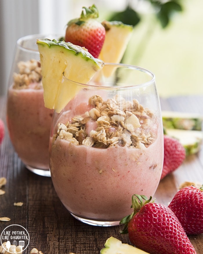 Two cups of strawberry pineapple smoothies topped with granola.