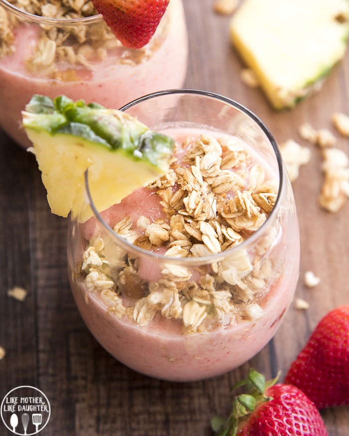An overhead photo of a pink smoothie topped with granola, with a pineapple wedge on the glass edge. 