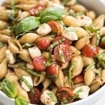 A close up of a bowl of caprese pasta salad with fresh basil on top.