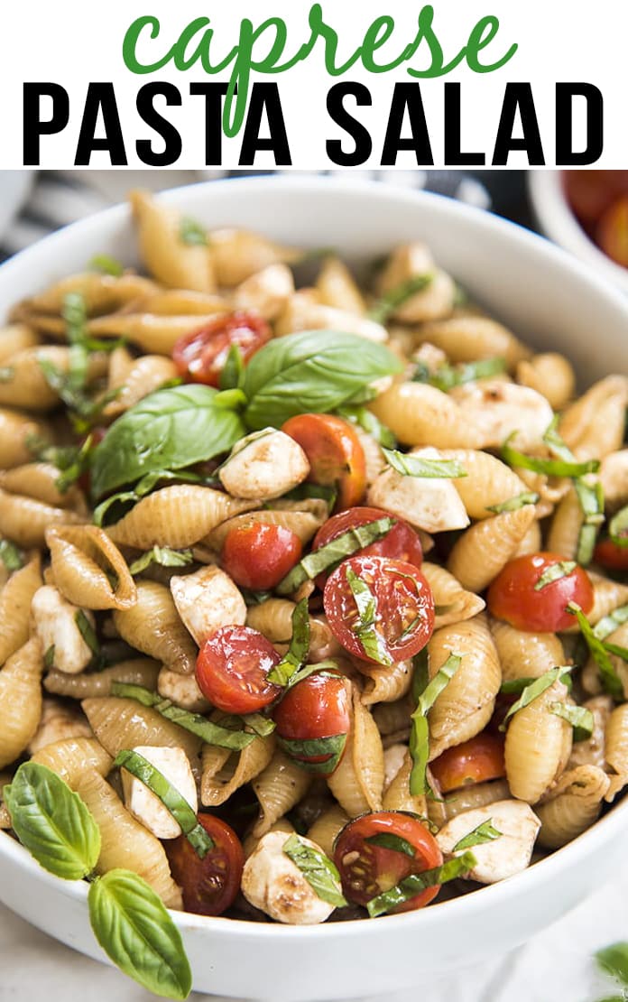 A close up of a bowl of caprese pasta salad with fresh basil on top.