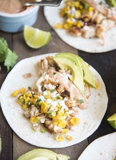 A chicken and mexican corn taco on a wooden board.