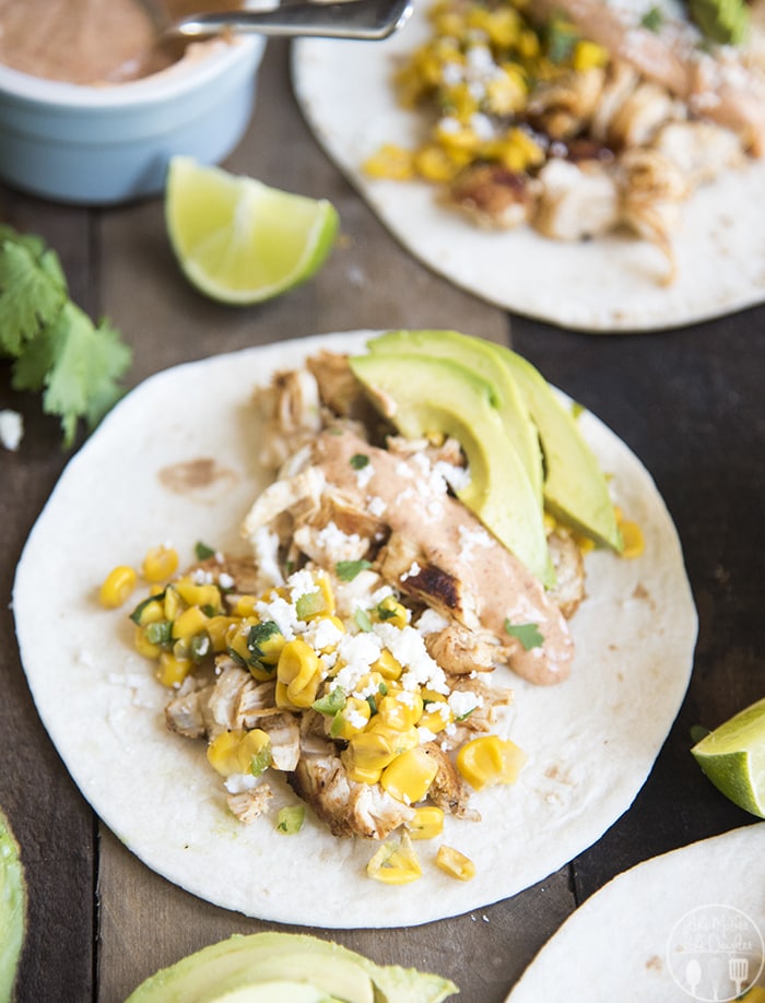A chicken and mexican corn taco on a wooden board.