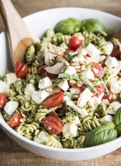 A bowl of pesto pasta salad with chicken and tomatoes.