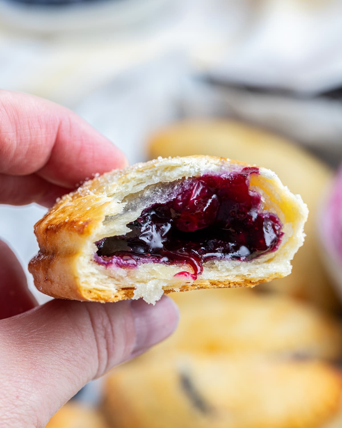 A hand holding a blueberry hand pie with a bite out of it, showing the blueberry filling.
