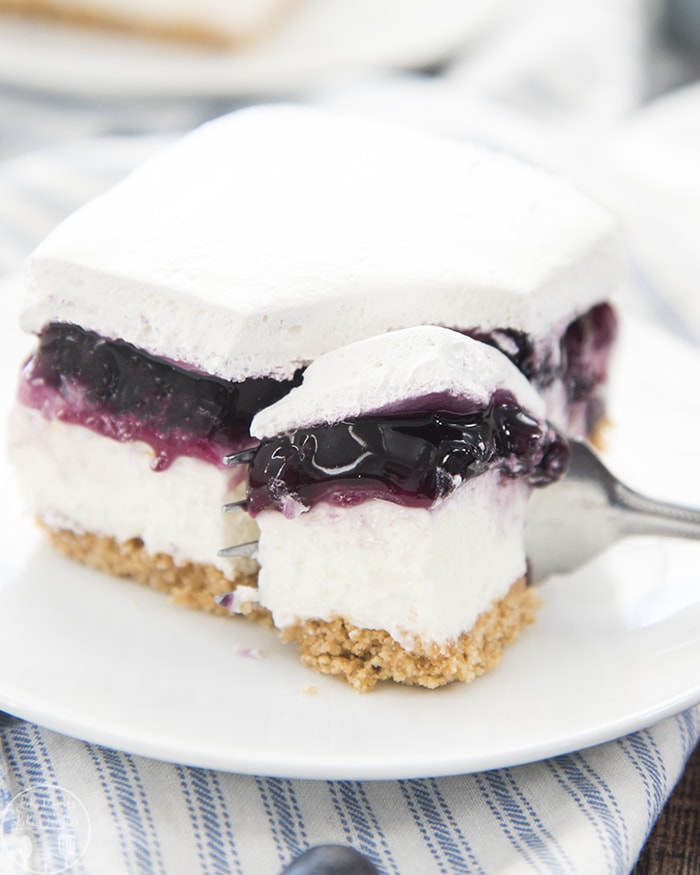 A piece of blueberry cheesecake bars with a fork cutting a portion out.